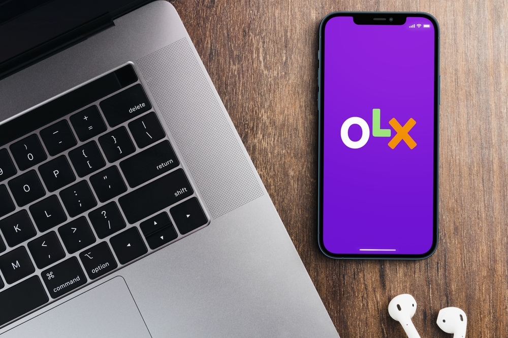 Imagem de um laptop, celular com logo OLX na tela e fones de ouvido brancos sobre uma mesa de madeira, otimizada para compra e venda de produtos na OLX.